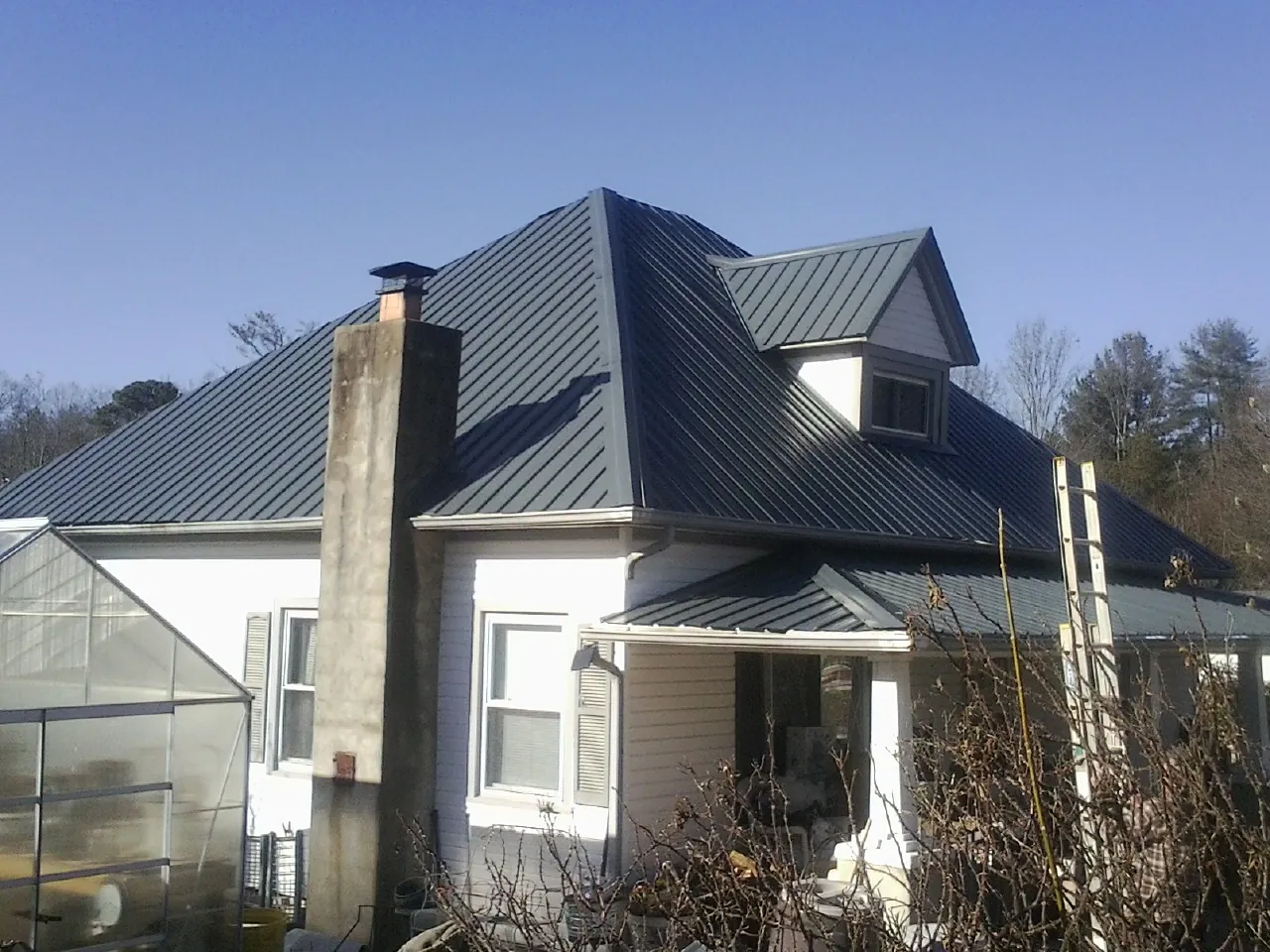 Dark blue standing seam metal roof on a white farmhouse with dormer — Slate & Tile Roof Repair by Roofing Brothers in Hensley