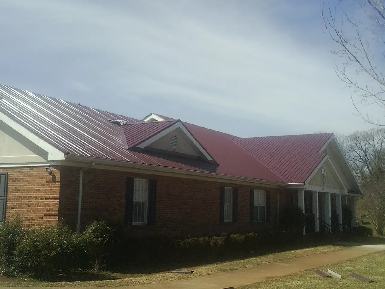 Red metal roof with gabled entries on a long brick building, from a Hail Damage Roof Repair job in Hensley