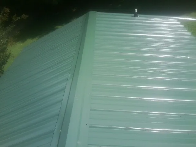 New green metal panels meeting at the ridge of a roof — Flat Roof Repair work by our crew in Hensley