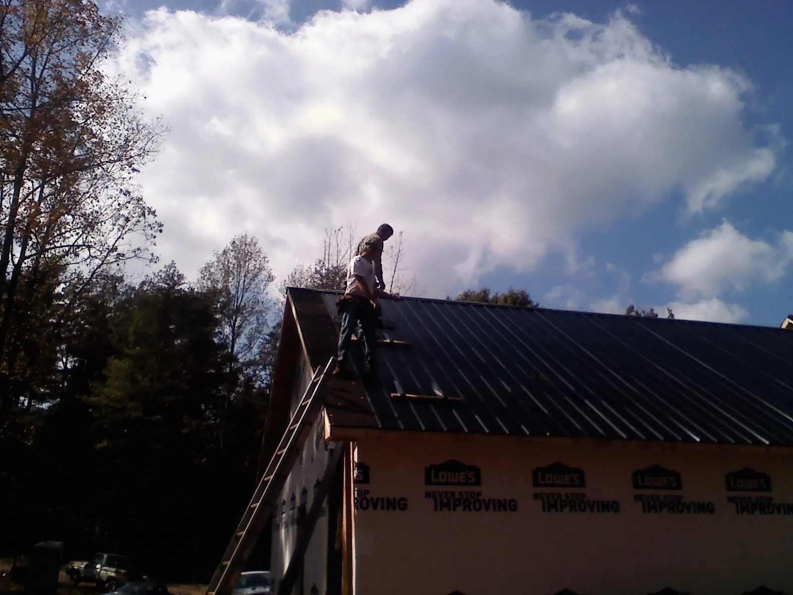 Roofer fastening dark metal panels high against a cloudy sky, from a Roof Inspection job in Hensley