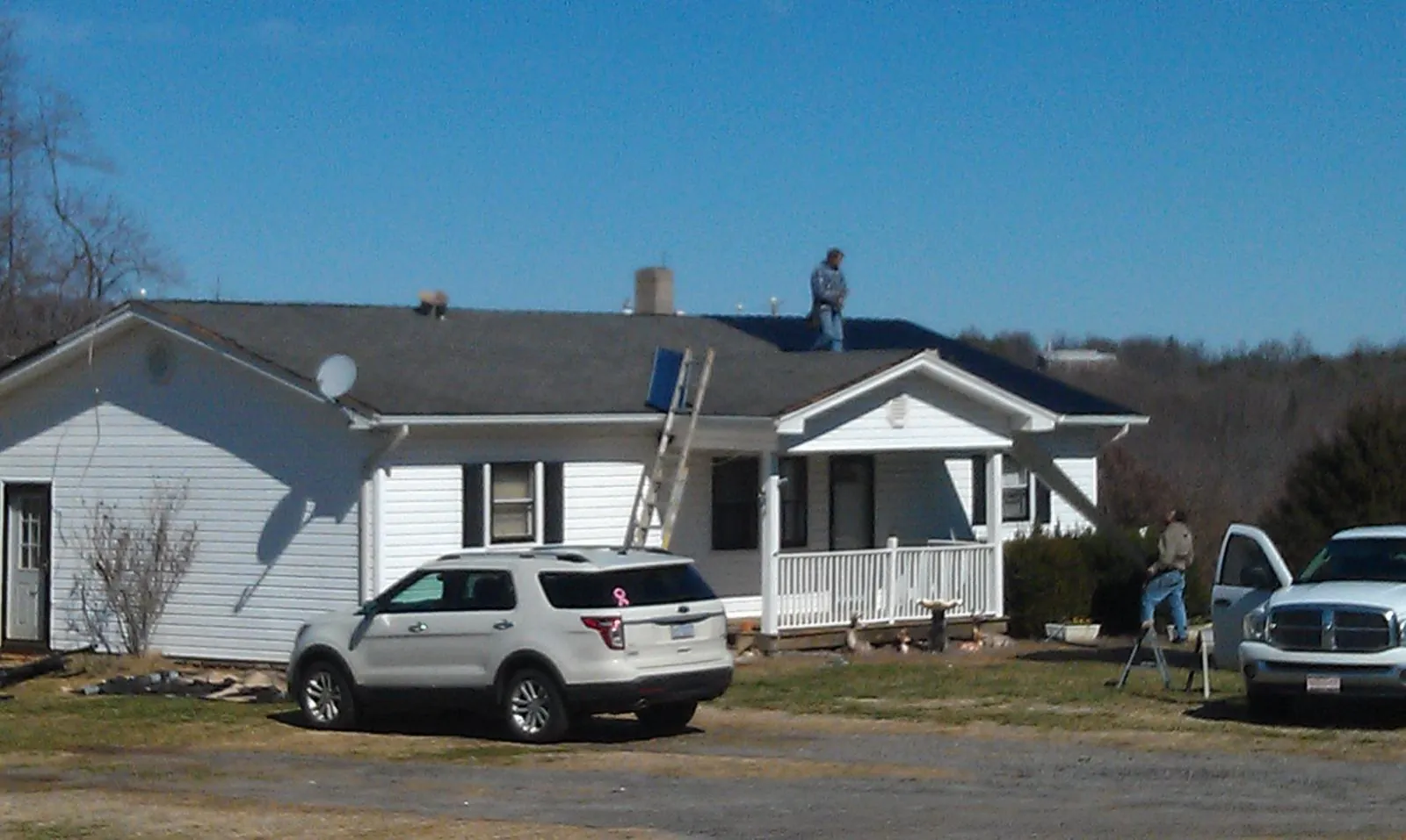 Roofers stripping shingles from a white ranch house roof in Hensley